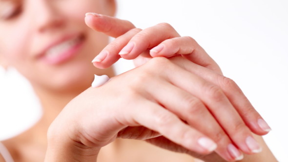 Smiling young woman applies cream on her hands. On a white background.